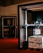 Robots apilando cajas en una fábrica con un cartel que dice "CAST Automation".