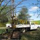 Truck-mounted drilling rig working in a grassy area surrounded by trees.