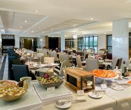 Restaurante elegante com mesas e buffet variado. Ambientes iluminados e decoração moderna.