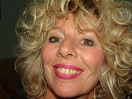 Eine Frau mit lockigem blondem Haar lächelt in die Kamera.