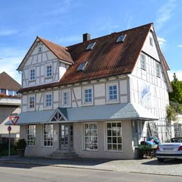 Fachwerkhaus mit rotem Dach unter blauem Himmel in einer ruhigen Straße.