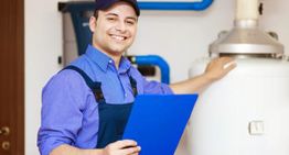 Tecnico sorridente con cappello blu tiene una cartellina vicino a un'apparecchiatura industriale.