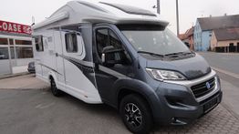 Grau-weißes Wohnmobil steht auf einem Bürgersteig, im Hintergrund sind Gebäude sichtbar.