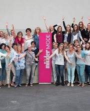 Gruppe von Frauen posiert fröhlich mit erhobenen Armen vor einem "müller MODE"-Schild.