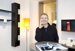 Eine Person sitzt in einem modernen Raum und lächelt, mit offenem Magazin vor sich auf dem Tisch.