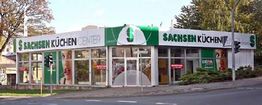 Eckgebäude mit Glasfronten und großem Schriftzug "Sachsen Küchen Center", Grün-Weiß gestaltet.