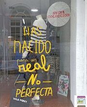 Escaparate con frase: "Has nacido para ser real, no perfecta". Ropa y cartel "Nueva Colección".