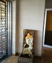 Busto de Buda decorativo en una esquina de una habitación con suelo de madera y puerta de rejilla.