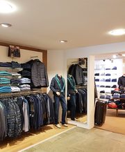 Kleidergeschäft mit Anzügen, Hemden und Pullovern auf Regalen und Kleiderständern.