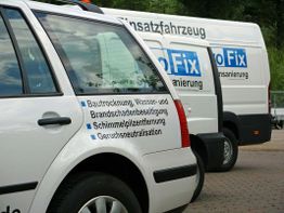 Zwei weiße Firmenfahrzeuge mit Werbung für Bautrocknung und Schadenssanierung stehen nebeneinander.