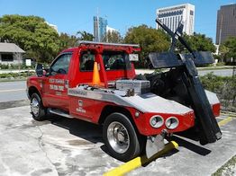 Red tow truck parked outdoors, with city buildings in the background.