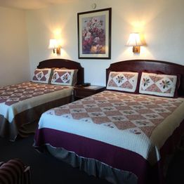 Two beds with quilted covers in a hotel room, decorated with wall sconces and a floral painting.