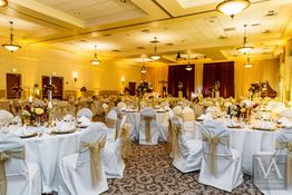 Elegant banquet hall with round tables, white chairs, floral centerpieces, and soft lighting.