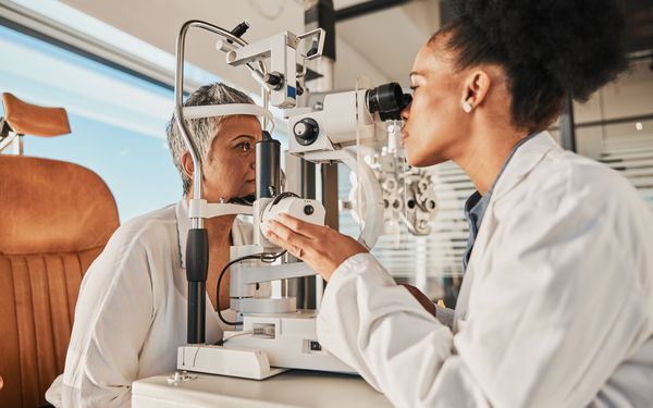 Eine Optikerin kontrolliert mittels eines Ophthalmoskop das rechte Auge ihrer Patientin zur Vorsorge.