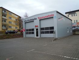 Kfz-Prüfstelle in Taunusstein, graues Gebäude mit Garagentoren, leerer Parkplatz davor.