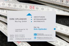 Visitenkarte von Dirk Opländer auf zusammengerolltem Maßstab liegend, mit Kontaktinfos.
