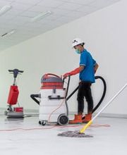 Arbeiter reinigen einen Boden mit Maschinen, vor einem Schild „Cleaning in Progress“ im Vordergrund.