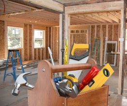 Wooden toolbox with tools in a house under renovation, ladders and wooden framing visible.