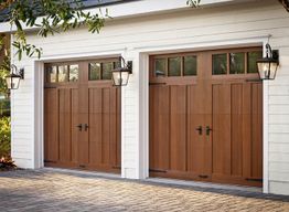 Two wooden garage doors with lantern-style lights on a white building.