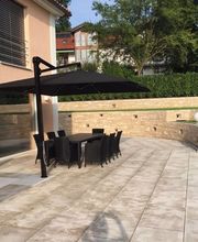 Moderne Terrasse mit Esstisch und Sonnenschirm, umgeben von Grün und Steinmauern.