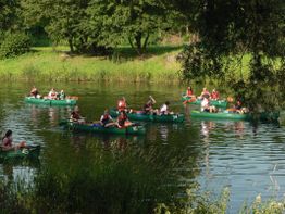 Menschen paddeln in grünen Kanus auf einem ruhigen Fluss, umgeben von grüner Natur.