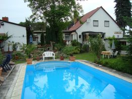 Haus mit Garten, Swimmingpool und Pflanzen; gemütlicher Außenbereich mit Bäumen und Möbeln.