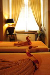 Zwei Betten mit kunstvoll gefalteten Handtüchern vor einem Fenster mit gelben Vorhängen.