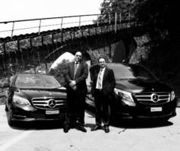 Zwei Männer stehen vor zwei Mercedes-Autos unter einer Brücke.
