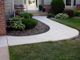Curved concrete path with shrubs and rocks leads to a front door.