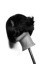 Manichino con capelli scuri e corti, inclinato su un lato, su sfondo bianco.