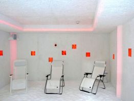 Drei Liegestühle in einem weißen Raum mit roten Lichteffekten an den Wänden.