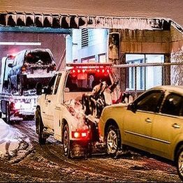Tow truck hauling a vehicle in a snowy urban setting with icicles hanging above.