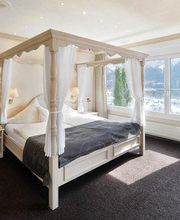 Helles Schlafzimmer mit Himmelbett, Vorhängen und Panoramafenster, Blick auf Berglandschaft.
