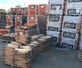 Pacchi di tegole e materiali edili impilati su pallet all'aperto.