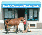 Eine Person tätowiert ein Pferd vor einem Studio mit blauem Schild.