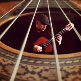 Blick durch Gitarrenseiten, ein Mann spielt konzentriert eine Gitarre.