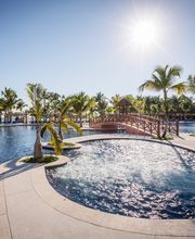 Piscina al aire libre con palmeras y puente de madera, bajo un cielo despejado y soleado.
