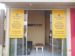 Fachada de escritório de arquitetura com placas amarelas e sofás na entrada.