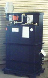 Ein großer, schwarzer Tank mit Rohren und einem Motor, vor einem gestreiften Metalltor.