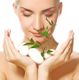 Frau hält weiße Steine mit grünen Blättern, Augen geschlossen, entspannte Gesichtsausdruck.