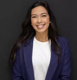 Smiling woman in a blue blazer and white top against a dark background.