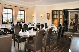 Gemütliches Restaurant mit gedeckten Tischen und braunen Stühlen, Tageslicht durch die Fenster.