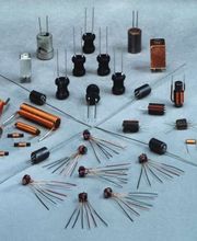 Verschiedene elektronische Bauteile, darunter Spulen und Kondensatoren, auf grauem Untergrund.