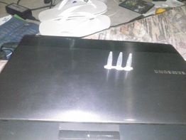 Um laptop Samsung com três objetos pequenos em cima.