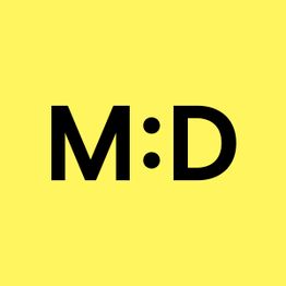 Schwarzer Text "M:D" auf gelbem Hintergrund.