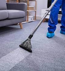 Person cleaning carpet with vacuum, showing visible dirt removal, beside a sofa.