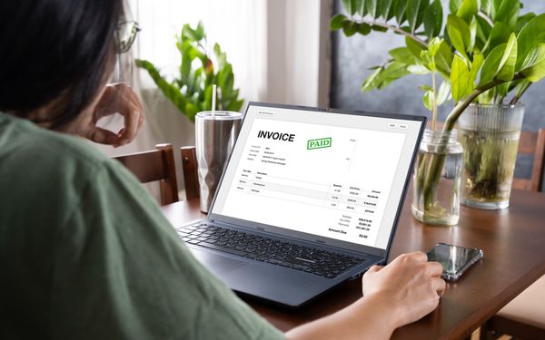Eine Frau in einer grünen Bluse sitzt vor ihrem Laptop auf dem eine E-Rechnung geöffnet zu sehen ist.