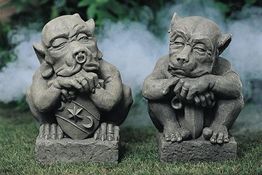 Zwei groteske Gargoyle-Statuen auf Gras, umgeben von leichtem Nebel.