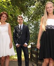 Drei elegant gekleidete Personen im Freien auf einer Brücke, umgeben von Bäumen.