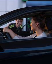 Mujer en auto sonríe al empleado en una gasolinera.
